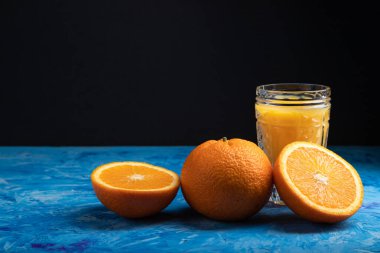 Siyah ve mavi arka planda bir bardak portakal suyu. Sert ışık, kontrast. Yan görünüm, boşluk kopyala.