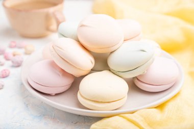 Renkli zephyr veya bir fincan kahveli marşmelov ve beyaz beton arka plan ve sarı tekstil üzerine sürükleyici. Yan görünüm, yakın görünüm, seçici odak.