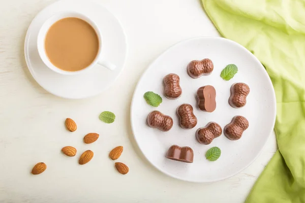 Caramelle Cioccolato Con Mandorle Una Tazza Caffè Sfondo Bianco Legno — Foto Stock