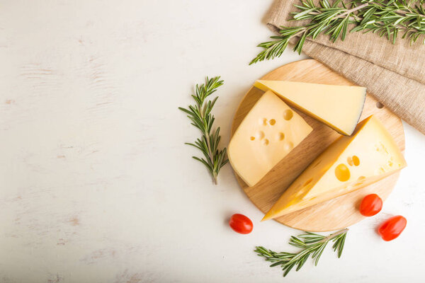 Various types of cheese with rosemary and tomatoes on wooden board on a white wooden background and linen textile. Top view, close up, copy space, flat lay.