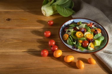 Pac choi lahana, kivi, domates, kumkatlı vejetaryen salatası, ahşap arka planda mikroyeşil lahanalar ve keten tekstil. Sert ışık, kontrast. Yan görünüm, seçici odak, kopyalama alanı.