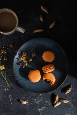 Siyah beton arka planda bir fincan kahveyle portakallı kurabiyeler veya kurabiyeler. Sert ışık, kontrast, düşük tuş. Üst manzara, düz yatak, yakın çekim..