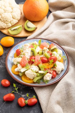 Vejetaryen lahana, kivi, domates, siyah beton arka planda mikroyeşil lahanalar ve keten tekstil salatası. Yan görünüm, kapat.