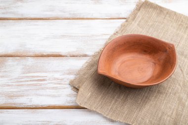 Beyaz ahşap zemin ve keten tekstil üzerine boş kil kahverengi kase. Yan görünüm, kapat, boşluğu kopyala.