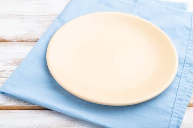 Beyaz ahşap arka planda boş seramik plaka ve mavi keten kumaş. Yan görünüm, kapat.