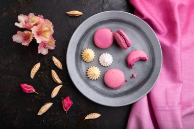 Mor badem kurabiyeleri ya da siyah beton arka planda bir fincan kahve ve pembe tekstil içeren badem kurabiyeleri. Üst manzara, düz yatak, yakın çekim..