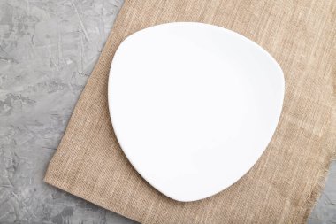 Gri beton arka plan ve keten tekstil üzerine boş beyaz plaka. Üst manzara, kapat, düz yat..