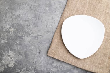 Gri beton arka plan ve keten tekstil üzerine boş beyaz plaka. Üst görünüm, kopyalama alanı, düz uzanma.