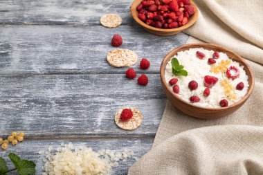 Pirinç lapası sütlü lapa ve ahşap kapta çilekli gri ahşap arka plan ve keten tekstil. Yan görünüm, boşluk kopyala.