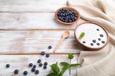 Beyaz ahşap arka planda yaban mersinli yoğurt ve keten tekstil. Yan görünüm, boşluk kopyala.