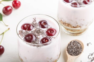 Kirazlı yoğurt, kiraz tohumu ve beyaz ahşap arka planda tahta kaşıkla cam içinde granola. Yan görünüm, kapat.