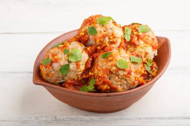 Domates soslu domuz köftesi, kekik yaprakları, baharatlar ve beyaz ahşap arka planda kil kasede otlar. Yan görünüm, kapat