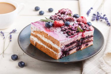 Sütlü kek ve mavi seramik tabakta yabanmersini reçeli, bir fincan kahve ve beyaz ahşap arka planda taze yaban mersini. Yan görünüm, yakın görünüm, seçici odak.