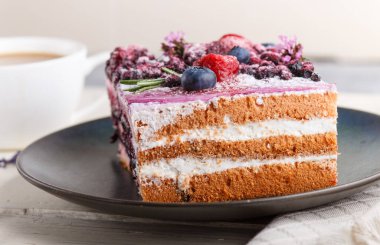 Sütlü kek ve mavi seramik tabakta yabanmersini reçeli, bir fincan kahve ve beyaz ahşap arka planda taze yaban mersini. Yan görünüm, yakın görünüm, seçici odak.