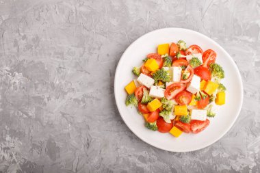 Brokolili vejetaryen salatası, domates, beyaz seramik tabakta beyaz seramik peynir ve gri arka planda balkabağı, üst manzara, fotokopi alanı, düz konum.