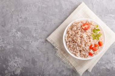 Beyaz kasede cilalanmamış pirinç lapası gri beton arka plan ve keten tekstil. Üst görünüm, düz görünüm, kopyalama alanı.