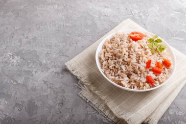 Cilalanmamış pirinç lapası haşlanmış sebzeler ve gri beton arka planda keklik otu ve keten tekstil. Yan görünüm, boşluk kopyala.