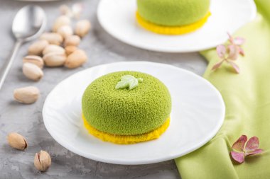 Fıstık kremalı yeşil kremalı kek ve gri beton arka planda bir fincan kahve ve yeşil tekstil. Yan görünüm, yakın görünüm, seçici odak.