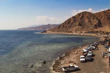 Kızıl Deniz 'in küçük tatil beldeleri ve arka planında dağlar olan kıyı şeridi. Mercan resifi Mavi Delik. Mısır, Sina Yarımadası, Dahab.