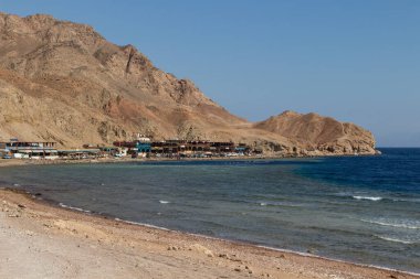 Kızıl Deniz 'in küçük tatil beldeleri ve arka planında dağlar olan kıyı şeridi. Mercan resifi Mavi Delik. Mısır, Sina Yarımadası, Dahab.