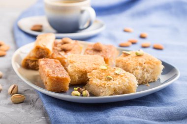 Geleneksel Arap tatlıları (basbus, kunafa, baklava) ve gri beton arka plan ve mavi tekstil üzerinde bir fincan kahve. Yan görünüm, yakın görünüm, seçici odak.
