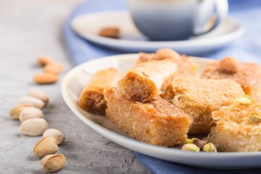 Geleneksel Arap tatlıları (basbus, kunafa, baklava) ve gri beton arka plan ve mavi tekstil üzerinde bir fincan kahve. Yan görünüm, yakın görünüm, seçici odak.