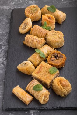 Siyah beton zemin üzerinde siyah bir tahta üzerinde geleneksel Arap tatlıları (kunafa, baklava). Yan görünüm, kapat.