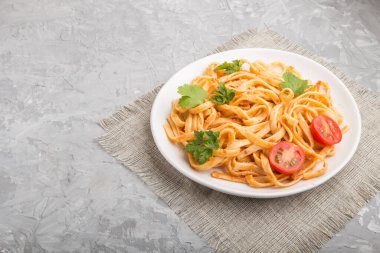 Domates soslu Semolina makarnası, turuncu ve otlar gri beton arka planda beyaz bir seramik tabakta. Yan görünüm, boşluk kopyala.