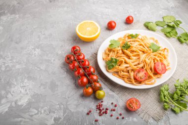 Domates soslu Semolina makarnası, turuncu ve otlar gri beton arka planda beyaz bir seramik tabakta. Yan görünüm, boşluk kopyala.