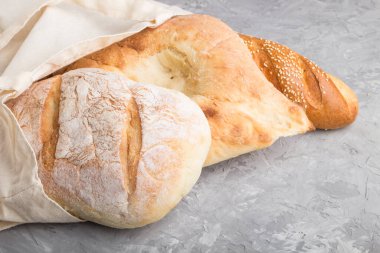 Gri beton arka planda taze pişmiş ekmek ile yeniden kullanılabilir tekstil bakkal torbası. Yan görüş, boşluğu kopyala. sıfır atık kavramı.