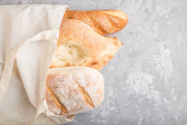 Gri beton arka planda taze pişmiş ekmek ile yeniden kullanılabilir tekstil bakkal torbası. Üst görünüm, düz görünüm, kopyalama alanı. sıfır atık kavramı.