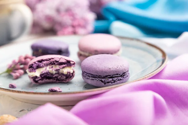 Purple macarons or macaroons cakes with cup of coffee on a white concrete background and magenta-blue textile. Side view, close up, selective focus.