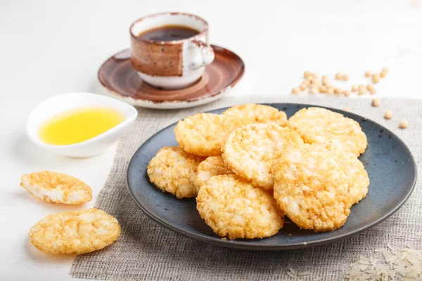 Geleneksel Japon pirinç cipsi kurabiyeleri, ballı ve soya soslu mavi seramik tabak ve beyaz ahşap arka planda bir fincan kahve. Yan görünüm, yakın görünüm, seçici odak.