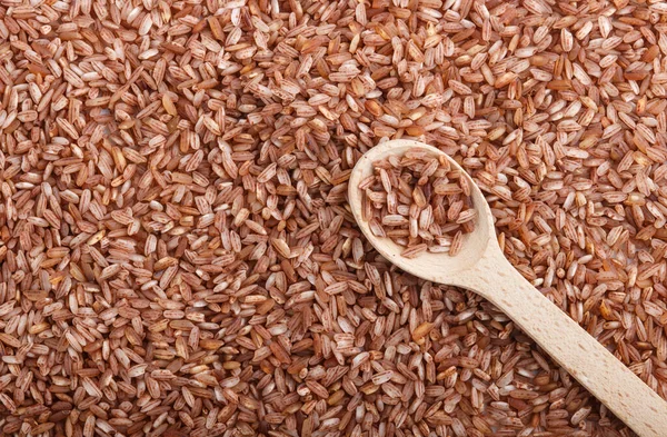 Texture of unpolished brown rice with wooden spoon. Top view, flat lay, close up, macro. Natural background.