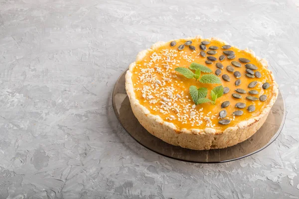 Traditional american sweet pumpkin pie decorated with mint, sesame and pumpkin seeds on a gray concrete background. side view, copy space.