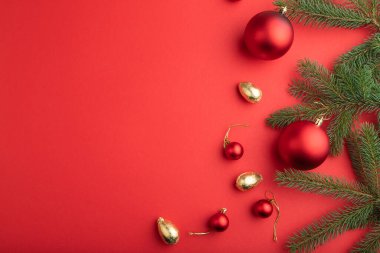 Noel veya Yeni Yıl kompozisyonu. Süslemeler, kırmızı toplar, köknar ve ladin dalları, kırmızı kağıt arka planda. Üst görünüm, kopyalama alanı, düz uzanma.