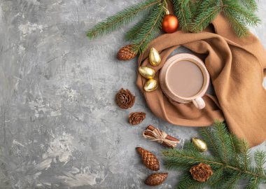 Noel veya Yeni Yıl kompozisyonu. Dekorasyonlar, koniler, tarçın, köknar ve ladin dalları, bir fincan kahve, gri beton arka planda yün atkı. Üst görünüm, kopyalama alanı, düz uzanma.