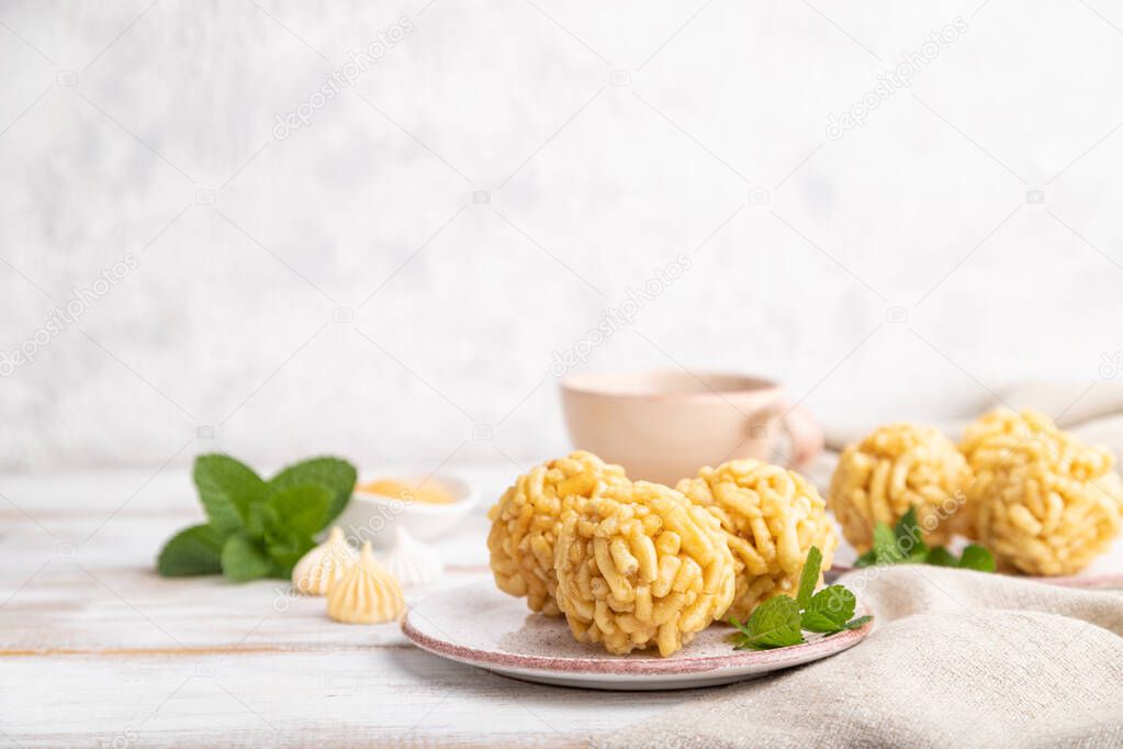 Traditional Tatar candy chak-chak made of dough and honey with cup of coffee on a white wooden background and linen textile. Side view, copy space, selective focus.