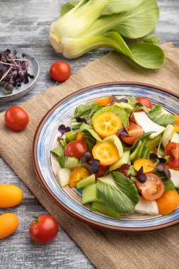 Pac choi lahana, kivi, domates, kumkatlı vejetaryen salatası gri ahşap arka planda mikroyeşil lahanalar ve keten tekstil. Yan görünüm, kapat.