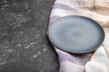 Siyah beton arka plan ve keten tekstil üzerine boş mavi seramik plaka. Yan görünüm, boşluk kopyala.