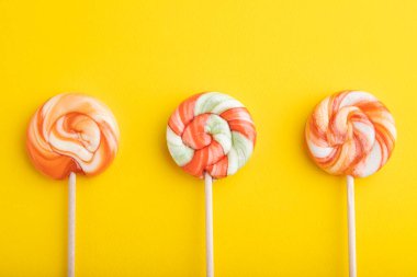 Sarı pastel arka planda üç lolipop şekeri. Boşluğu kopyala, üst görünüm, düz uzanma.