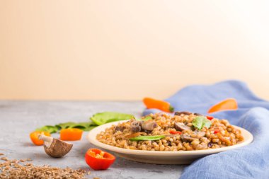 Gri ve turuncu arka planda seramik tabakta sebze ve mantarlı yulaf lapası ve mavi keten kumaş. Yan görüş, kopyalama alanı, seçici odaklanma. Rus geleneksel mutfağı.