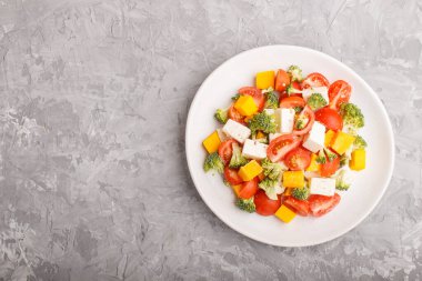 Brokolili vejetaryen salatası, domates, beyaz seramik tabakta beyaz seramik peynir ve gri arka planda balkabağı, üst manzara, fotokopi alanı, düz konum.