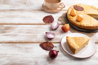 Sonbahar soğanlı turta, yapraklarla süslenmiş ve beyaz ahşap arka planda bir fincan kahve ve keten tekstil. Yan görünüm, boşluk kopyala.