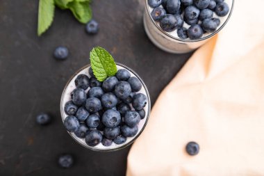 Siyah beton arka planda yaban mersinli yoğurt ve camlı chia ve turuncu keten kumaş. Üst görünüm, düz görünüm, yakın çekim.