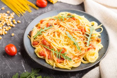 Siyah beton arka plan ve keten tekstil üzerine domates soslu mısır eriştesi ve roka. Yan görünüm, yakın görünüm, seçici odak.