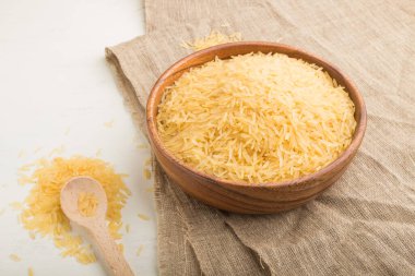 Tahta kase, çiğ altın pirinç, ahşap arka planda tahta kaşık ve keten tekstil. Yan görünüm, kapat.