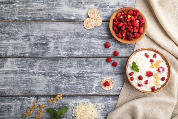 Rice flakes porridge with milk and strawberry in wooden bowl on gray wooden background and linen textile. Top view, flat lay, copy space.