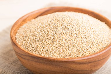 Beyaz ahşap arka planda çiğ beyaz kinoa tohumları ve keten tekstil ile ahşap kase. Yan görünüm, yakın görünüm, seçici odak.