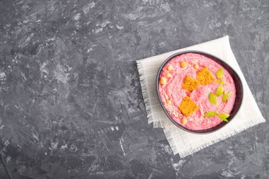 Siyah beton arka plan ve keten tekstil üzerinde seramik kasede pancar ve mikroyeşil fesleğen filizli humus. Üst görünüm, düz görünüm, kopyalama alanı.